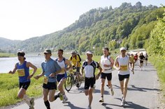 Teilnehmer aus einem vergangenen Oberelbe-Marathon laufen bei Sonnenschein und warmem Frühlingswetter am Elbufer des Festung Königstein entlang.
