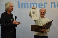 Waldemar Cierpinski zeigt sein Blatt, auf dem er sich im Goldenen Buch der Marathon Hall of Fame des LTL verewigt. Daneben steht Manfred Grüneberg.