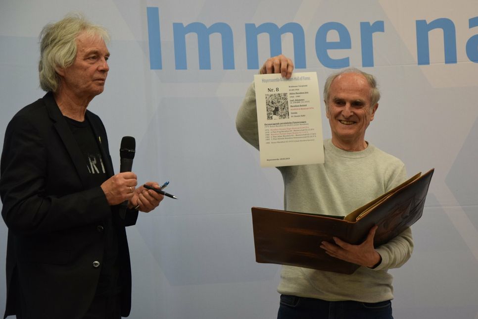 Waldemar Cierpinski zeigt sein Blatt, auf dem er sich im Goldenen Buch der Marathon Hall of Fame des LTL verewigt. Daneben steht Manfred Grüneberg.
