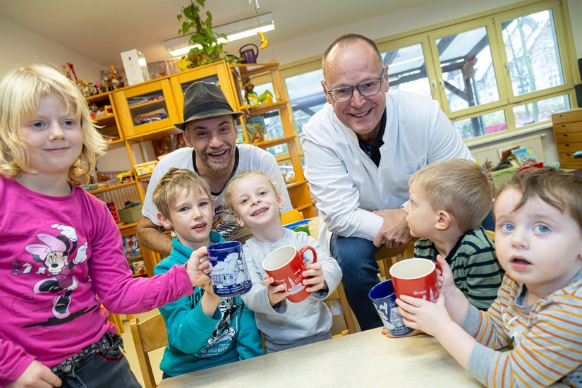 Cartoonist Kümmel (links) und Apotheker Heiko Neumann besuchen die Gruppe 1 im Kindergarten Pusteblume. Im vergangenen Jahr gab’s die große rote Tasse auf dem Weihnachtsmarkt. Diesmal ist es die neue, blaue Tasse.