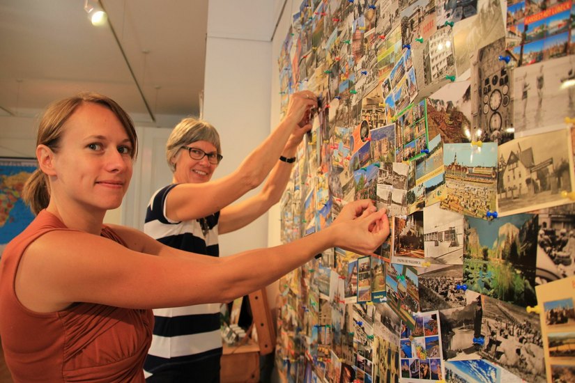 V.l. Katrin Kynast und Evelies Baumann vom Museum Karrasburg pinnen Urlaubskarten aus der ganzen Welt an.