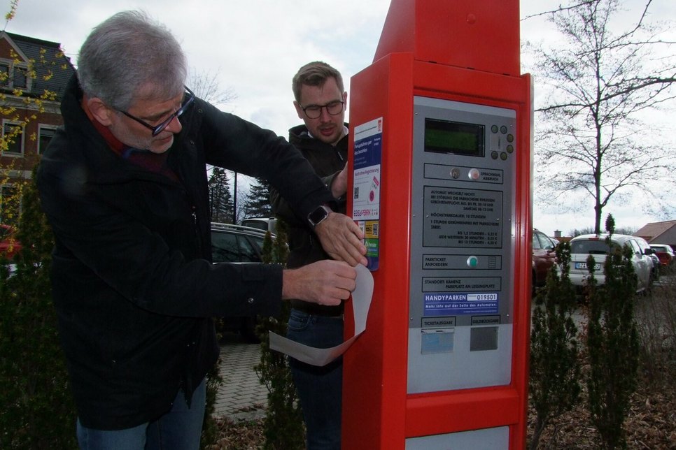 Ordnungsamtsleiter Joachim Hoyer (l.) und Christian Hartmann rüsteten am Montag die beiden Parkscheinautomaten auf. Aufkleber weisen Autofahrer darauf hin, dass man die Tickets per Smartphone buchen kann.