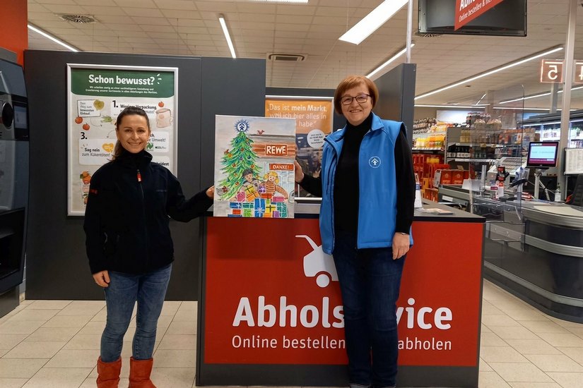 Heidi Kempke (re.) vom Deutschen Kinderschutzbund e.V., Ortsverband Senftenberg, überreicht Kerstin Radke (li.) vom Rewe-Markt in Senftenberg ein Aquarell. Das Motiv fasst die gemeinsame Weihnachtsaktion zusammen und ist ein Dank für die gute Zusammenarbeit.