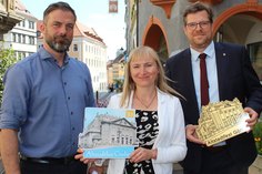 Kulturservice-Prokurist Gerd Weise, Kulturservice- Geschäftsführerin Maria Schulz und Bürgermeister Benedikt M. Hummel präsentieren das Motiv des Altstadtfest-Pins 2023.