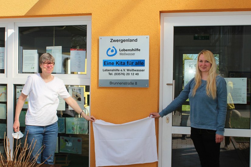 Kitaleiterin Kathrin Thöns und Susanne Kotte vom Elternrat enthüllen das neue Schild an der Kita. Foto: T. Keil