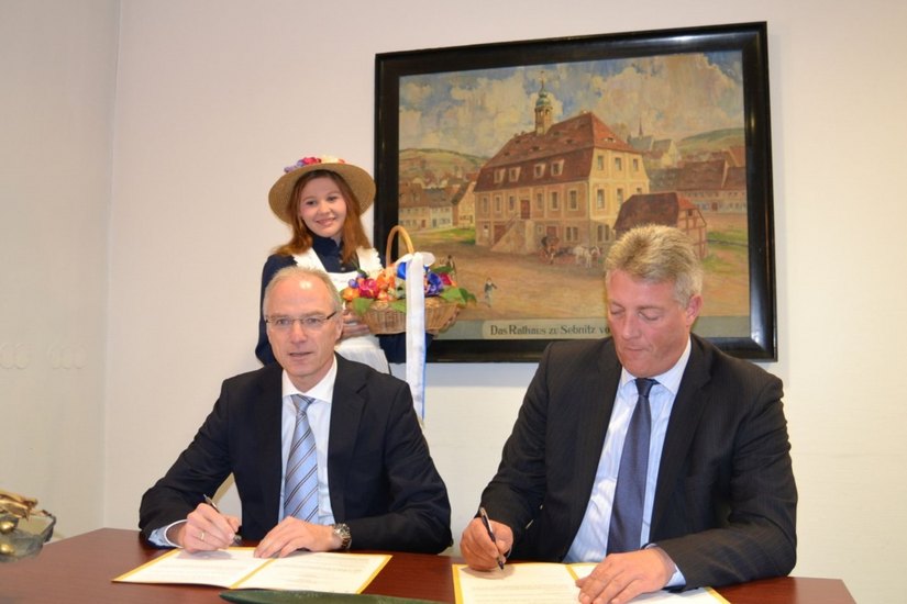 Volksbankchef Dr. Hauke Haensel (re.) und OB  Mike Ruckh unterzeichnen im Beisein des Sebnitzer Blumenmädchens Doreen Berger den Vertrag.                 Foto: SV