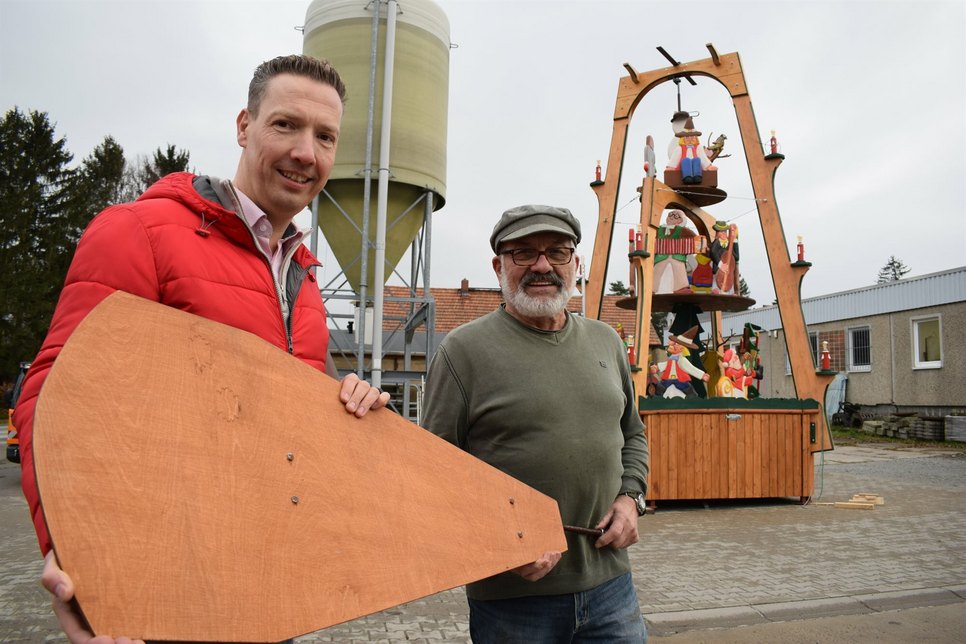 Bürgermeister Michael Herfort (links) und der Holzkünstler Jürgen Spottke haben einen Flügel der Weihnachtspyramide in der Hand. Die Flügel sowie das Dach werden in den nächsten Tagen noch montiert.