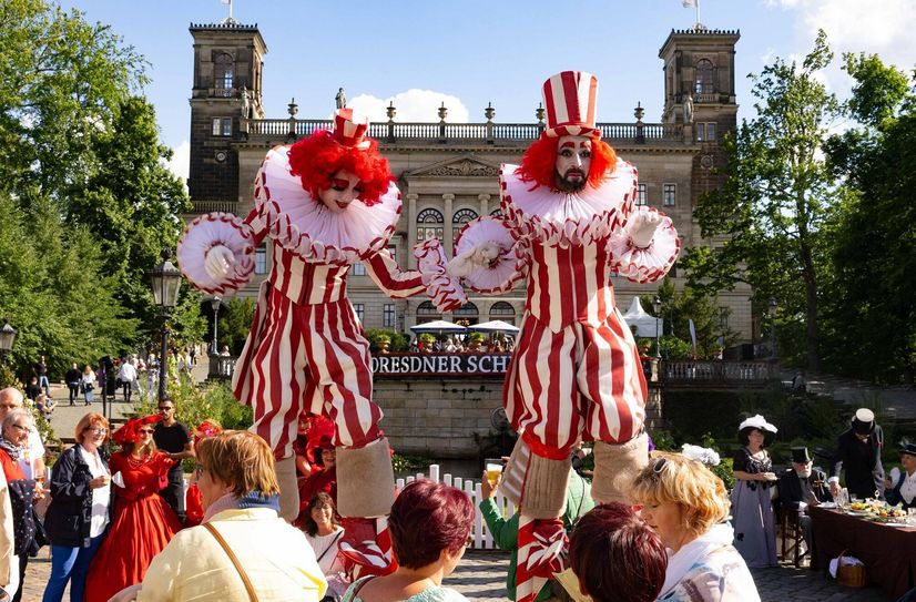 Stelzenläufer erfreuen das staunende Publikum vor der romantischen Schlösserfassade.