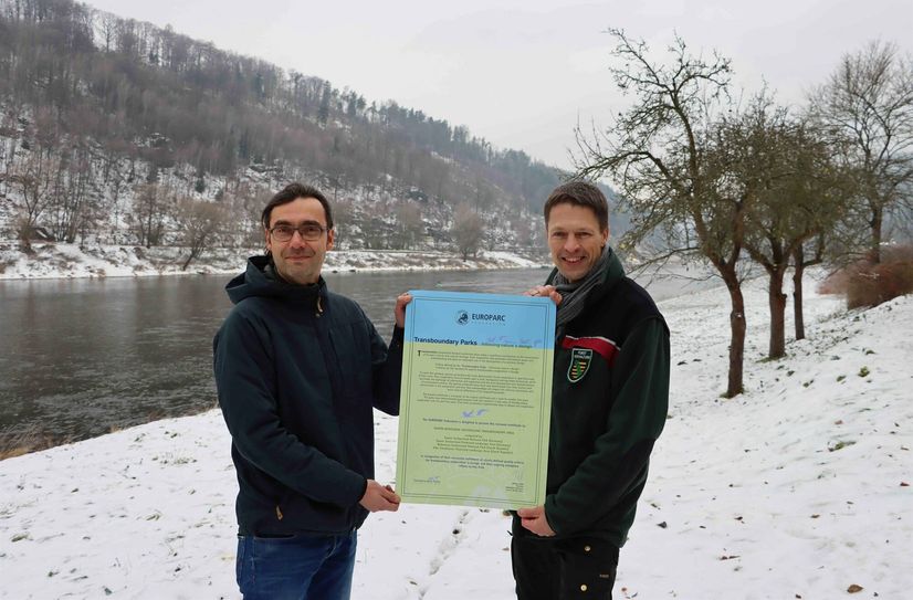 Am Ufer der Elbe, die alle vier Schutzgebiete in der Nationalparkregion Sächsisch-Böhmische Schweiz verbindet, präsentieren die Leiter der Nationalparkverwaltungen, Petr Kríž (li.) und Ulf Zimmermann, die Zertifizierungsurkunde.