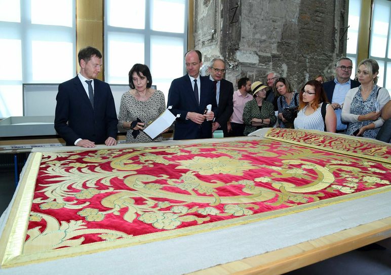Ministerpräsident Kretschmer begutachtet die Bettdecke, die einst auf dem Prachtbett im Schlafgemach des Kronprinzen lag  Foto: Wolf