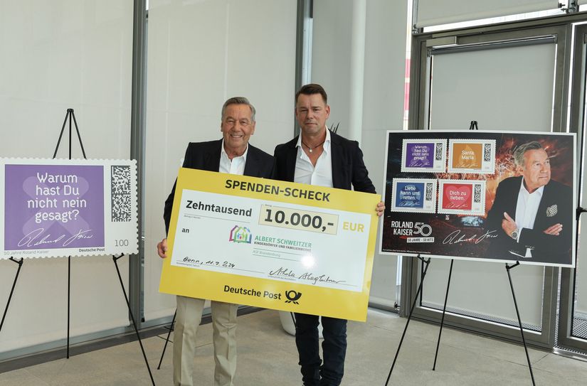 Roland Kaiser und Kai Noack bei der Spendenübergabe im Bonner Post Tower. Im Hintergrund ist die Briefmarken-Sonderedition zu sehen.