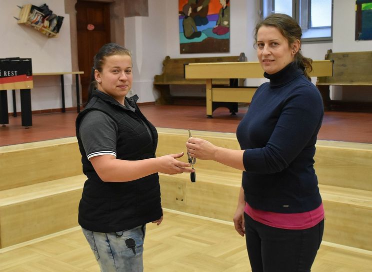 Brita Hanschmann übergibt symbolisch den Schlüssel und damit die Leitung des KAFF an ihre Nachfolgerin Theresa Kluge. Beide stehen im Hauptraum des KAFF, der vielfältig genutzt werden kann, dank des eingelassenen Fußbodens, sogar zum Fußball- und Jägerballspielen mit einem Softball. Foto: Trache