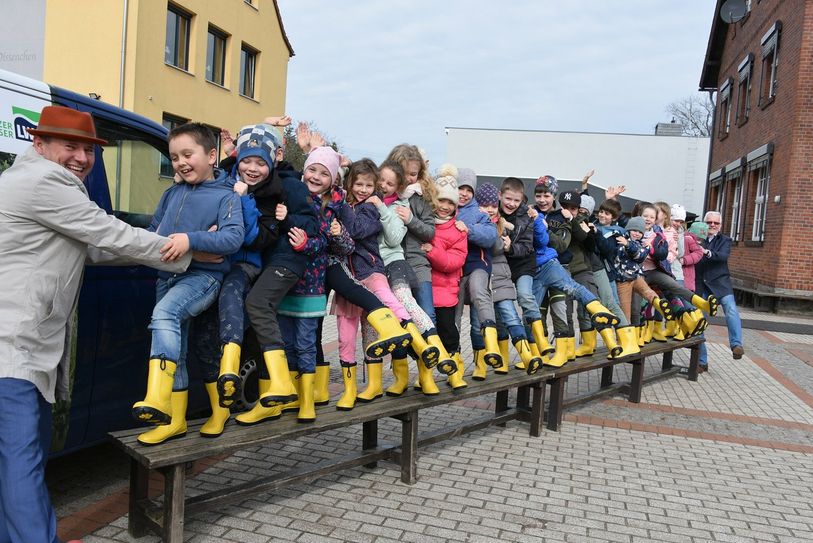 Die beiden LWG-Geschäftsführer Marten Eger (li.) und Jens Meier-Klodt übergeben knallgelbe Gummistiefel an die Schüler der Wassergenerationenklasse 2a der Umweltschule Dissenchen.
