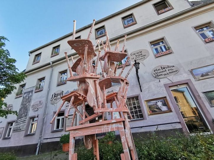 Beim Aufräumen fanden sich auf den Speichern des Dorfes 12 Stühle und ein Tisch des alten Gasthofes Serkowitz. Nun ist das Mobiliar als „Comeback“ wieder zurück gekehrt an seinen Ursprung und steht als Skulptur vor dem historischen Gemäuer des Lügenmuseums. Foto: Zabka