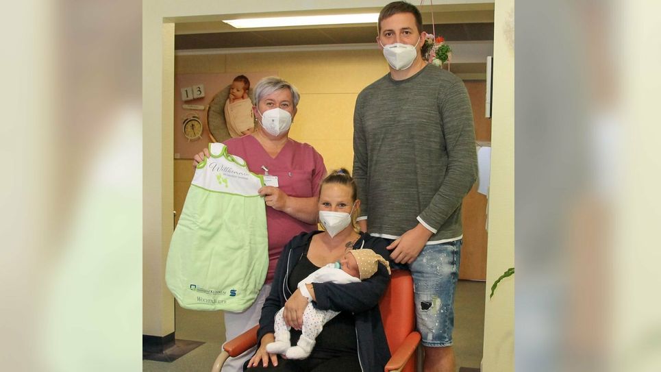 Hebamme Sabine Waschulewski (li.) überreicht den Eltern von Baby Nelio den ersten Schlafsack als Willkommens-Geschenk.