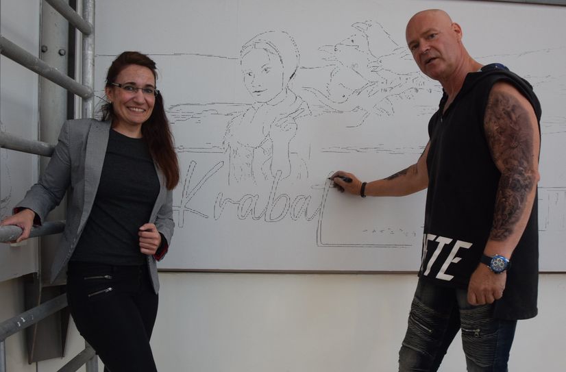 Madeleine Matschke und Jörg Tausch stehen auf dem Gerüst vor einem vorgezeichneten Teil des Wandbildes. In mehreren Nachtschichten des Künstlers nimmt es Form an.