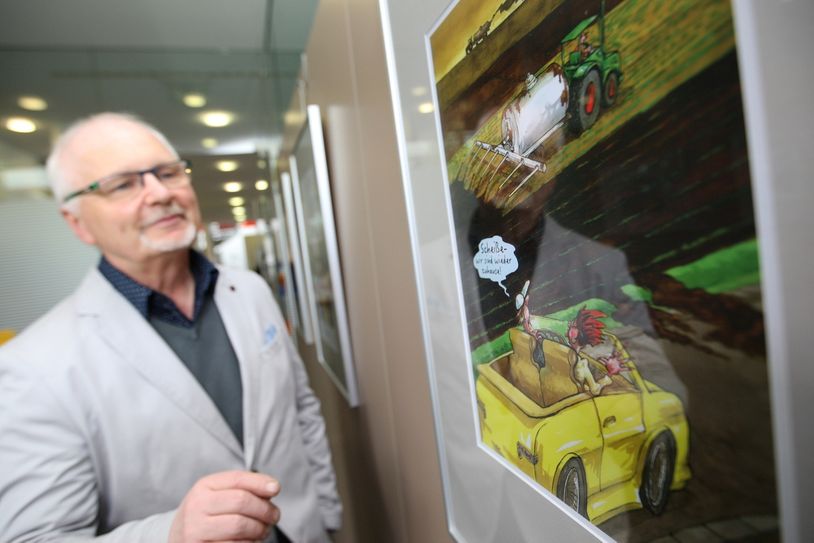 Der Pirnaer Herrenausstatter und Schneidermeister Eckhard Gnauk schaut sich eine von 80 Karikaturen in der Volksbank Pirna an und muss schmunzeln. "Scheiße – wir sind wieder zuhause" heißt es auf dem Bild. Foto: D. Förster