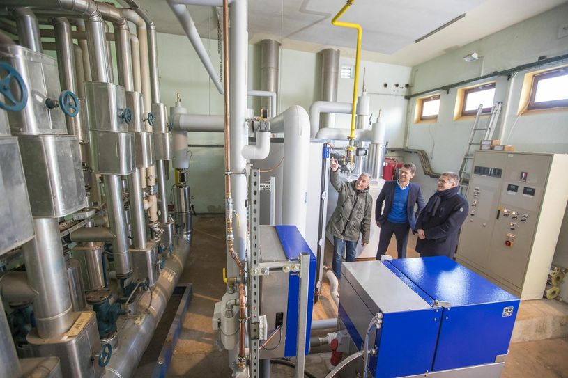 Schulleiter Harald Schmoz, ENSO-Kommunalvertriebsleiter Gunnar Schneider und Weinböhlas Bürgermeister Siegfried Zenker in der neuen Energiezentrale der Oberschule (vorn im Bild das BHKW).                                Foto: Enso