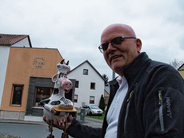 Bäckermeister Steffen Böhme vor seinem Grünberger Ladengeschäft. Seine Bäckerei ist in den Sommermonaten für Wanderer und Radler ein beliebter Anlaufpunkt, hier legen viele einen Pausenstopp ein. Und sind immer wieder von der kleinen Keramikkuh angetan, die ein örtlicher Künstler vor Böhmes Backgeschäft aufstellte.