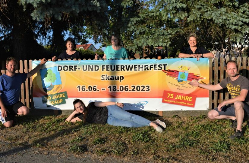 Einige Mitglieder des Skauper Organisationsteams am Werbeplakat am Ortseingang aus Richtung B 101.