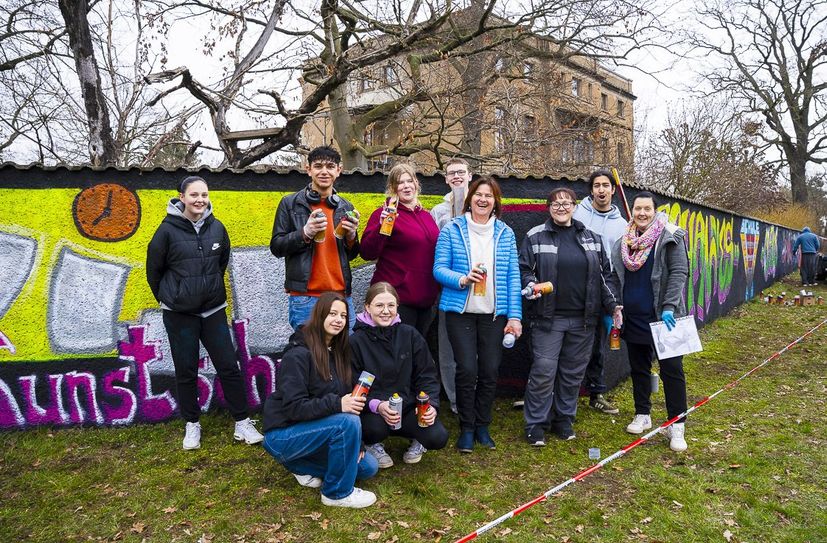 Teilnehmer des Graffiti-Projekts direkt am Kunstobjekt Mauer an der B87 Leipziger Straße/ Ecke Kaxdorfer Weg in Herzberg mit der Leiterin des Fachbereichs Kunst an der Kreismusik- und Kunstschule Gebrüder Graun, Gabi Lang (M).