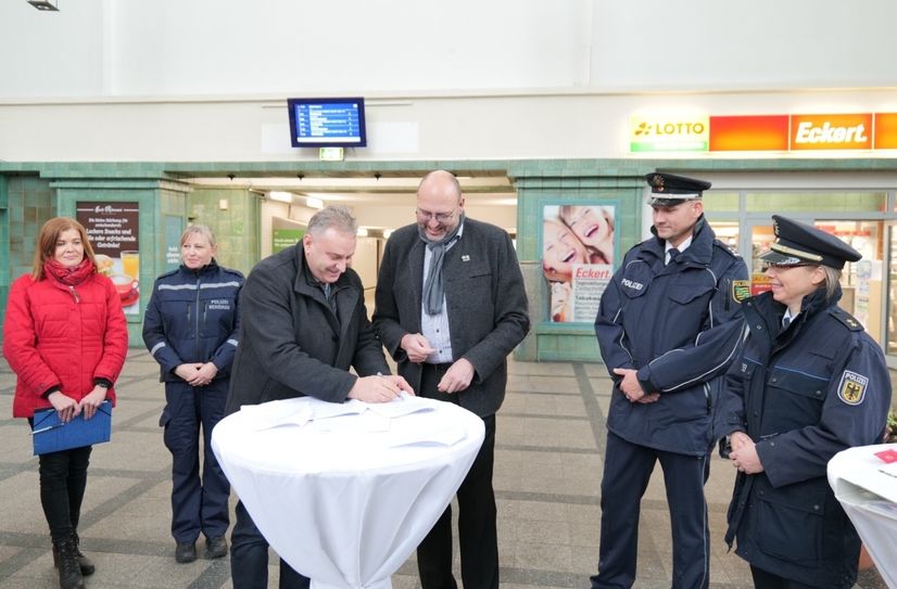 Heiko Klaffenbach, Leiter DB Bahnhofsmanagement Dresden und Meißens Oberbürgermeister Olaf Raschke (Mitte v.l.) unterzeichnen die Vereinbarung über die Sicherheits- und Ordnungspartnerschaft. Ebenfalls im Bild: Ordnungsamtsleiterin Belinda Zickler (in rot) sowie Kollegen von Bundes- und Landespolizei und Polizeibehörde, die künftig mit vereinten Kräften für Ordnung und Sicherheit im und um den Bahnhof sorgen werden.