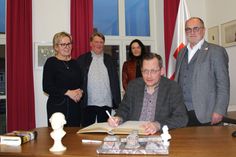 Clemens Meyer (sitzend) trägt sich im Beisein von Staatsministerin Barbara Klepsch (l.) sowie der Förderpreisträger Georg Genoux und Tina Pruschmann und Oberbürgermeister Roland Dantz (r.) ins Goldene Buch der Stadt Kamenz ein.
