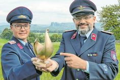 Die Feuerwehrmänner Toni Schulze (li.) und Kai Bigge mit der Goldenen Henne vor einem Panorama in der Sächsischen Schweiz.