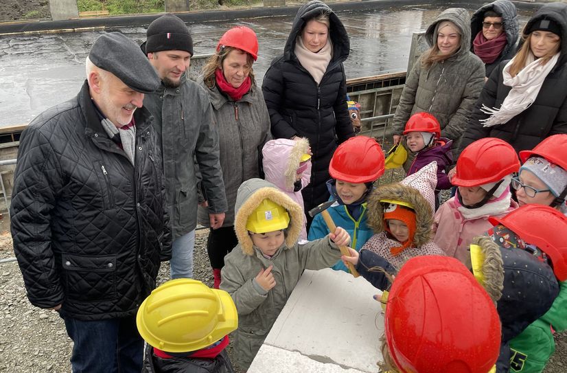Die Grundsteinschatulle ist bereits versenkt. Mit einem kleinen Hammer klopfen hier Kinder der Kita »Spatzennest« noch einmal symbolisch auf die Steine. Bürgermeister Thomas Zenker (li.), André Lehnick (2.v.li., Vorsitzender der Stadtverordnetenversammlung Großräschen) und Andrea Pohland (3.v.li., Einrichtungsleiterin der Kita »Spatzennest« in Großräschen) freuen sich über diese Hilfe.