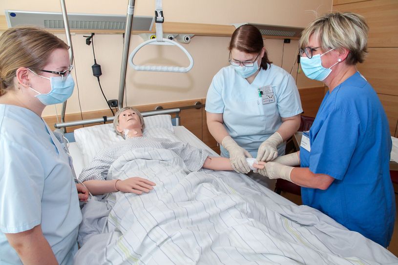 Praxisanleiterin Astrid Winkler übt mit den Schülerinnen Sina und Josephine das korrekte Wechseln eines sterilen Flexülenverbandes (v.r.), Foto: LSK/Gernot Schweitzer