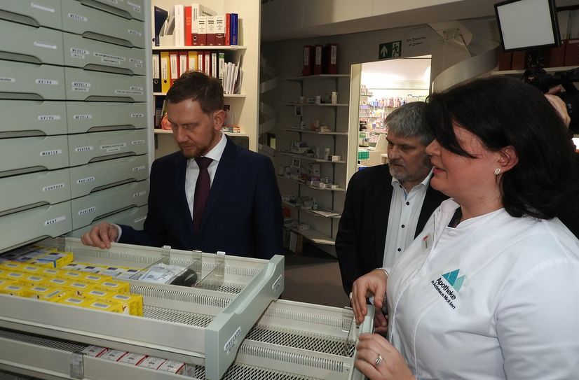 Ministerpräsident Michael Kretschmer, Apothekerverbandschef Thomas Dittrich und Apothekeninhaberin Maret Hoffmann (v. l. n. r.) schauen besorgt in leerer werdende Apothekerschränke.