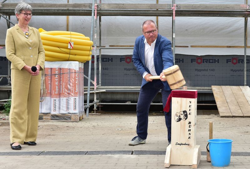 Kathrin Schneider (l.), Ministerin und Chefin der Staatskanzlei und Daniel Ris (r.), Intendant der neuen Bühne, schlagen einen symbolischen Holzpflock zum Richtfest des neuen Werkstattgebäudes ein.