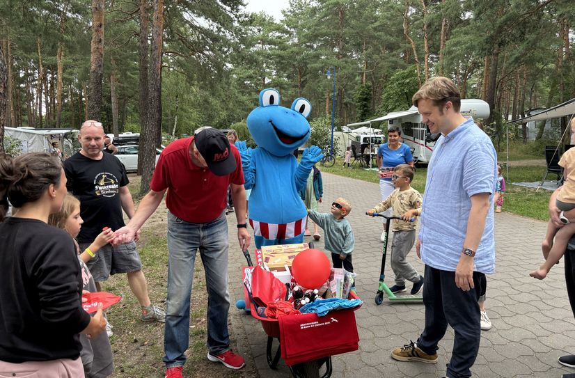 Mit Froggi und der roten Schubkarre hat die Campingplatz-Tour des Landesmarketing auch im Familienpark am Senftenberger See Halt gemacht. Bürgermeister Andreas Pfeiffer (r.) nutzte die Gelegenheit, mit den Seeurlaubern beim Frühstück ins Gespräch zu kommen.