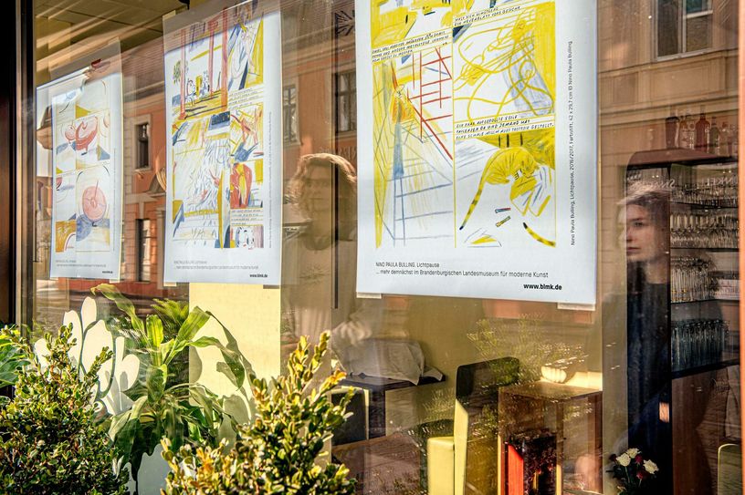 Passanten spiegeln sich im Schaufenster des Restaurants »bay´s« beim Betrachten von Plakaten aus der Graphic Novel »Lichtpause«. Foto: © Marlies Kross