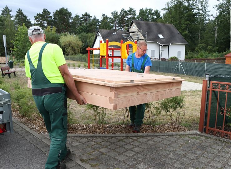 Bauhofmitarbeiter setzen den Sandkasten an seinen Bestimmungsort.