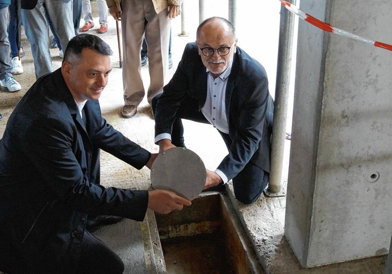 Udo Witschas und Roland Dantz (v.l.) lassen die Zeitkapsel in den Boden des Schulerweiterungsbaus ein. Foto: LRA Bautzen