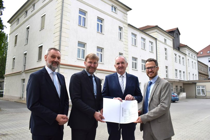 Der Umbau des ehemaligen Laborgebäudes im Hintergrund kann dank der der Fördermittelübergabe beginnen.Von links: Landtagsabgeordneter Marko Schiemann, OLK-Geschäftsführer Jörg Scharfenberg, Staatsminister Thomas Schmidt und Geschäftsführer der Oberlausitz Pflegeheim &amp; Kurzzeitpflege gGmbH, Sascha Bock.