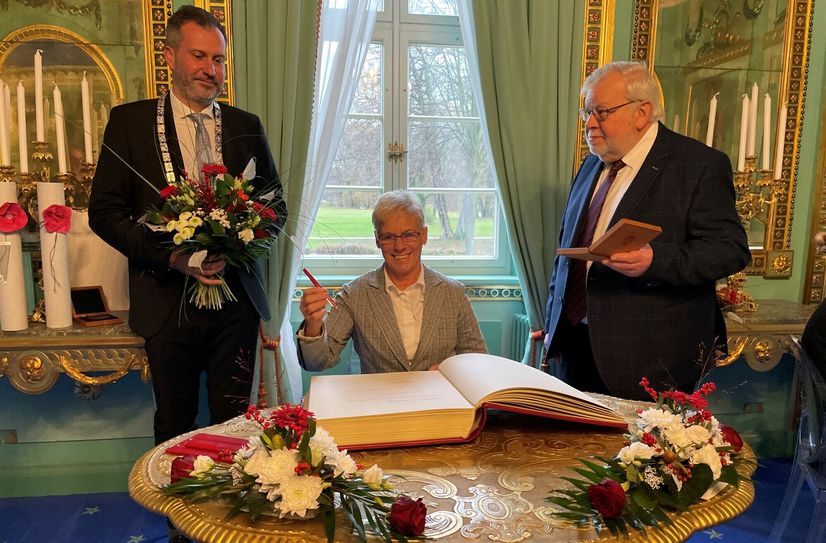 Elke Nowack trägt sich als Trägerin der Ehrenmedaille 2023 in das Goldene Buch der Stadt Cottbus ein, flankiert von OB Tobias Schick (l.) und dem 1. Stellvertreter des Vorsitzenden der Stadtverordnetenversammlung, Klaus Groß.