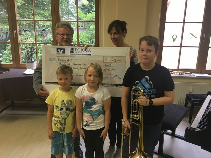 Katrin Heyde, Leiterin der Musikschule Außenstelle Sebnitz/Neustadt, nimmt gemeinsam mit Schülern den Scheck von Gunter Claus entgegen.   Foto: Dehoga