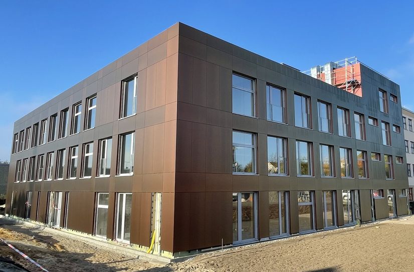 Der Anbau an der Regenbogen-Grundschule ist mit einer effektvollen, chamäleonartigen Fassade umhüllt. Je nachdem, aus welcher Richtung man das Gebäude betrachtet und je nach Stand der Sonne glänzt die Außenhaut des Neubaus in unterschiedlichen warmen Brauntönen.
