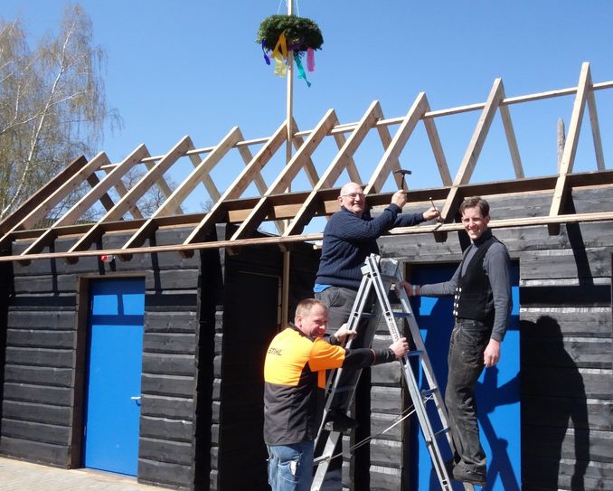 Bürgermeister Dreger schlägt symbolisch den letzten Nagel in den Dachstuhl ein. Die Bauhofmitarbeiter Guido Lichtenberger (li.) und Oliver Lehmann (re.) geben den WC-Containern ein spreewaldtypisches Aussehen. Foto: K. Möbes