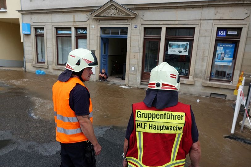 Frederik (9) hockt am Eingang eines Wohnhauses und sieht den aufgewühlten Schlamm vorbei fließen, während Feuerwehrleute das Areal absperren. Fotos: D. Förster