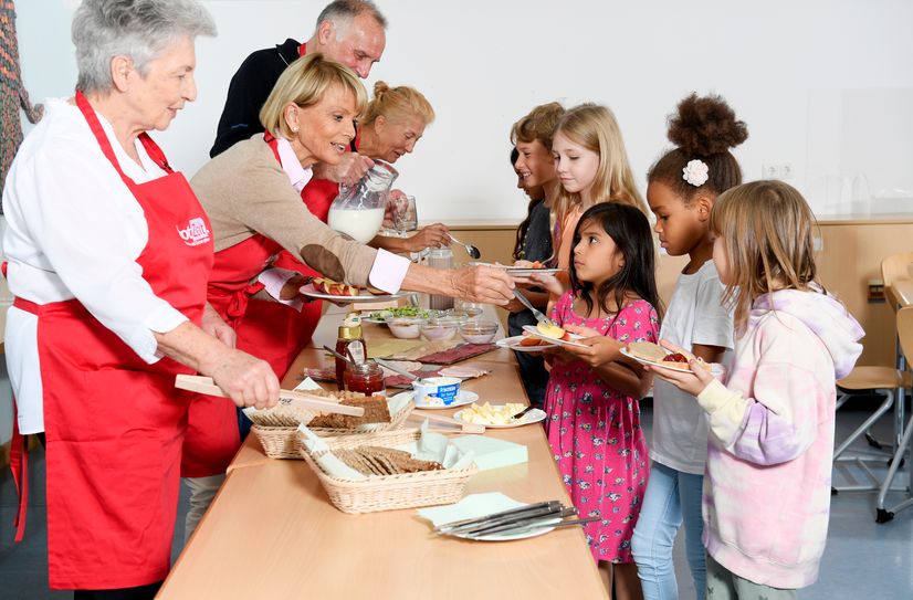 Engagierte Senioren und Schauspielerin Uschi Glas (2. v. li.) bereiten ein leckeres Frühstück für Schüler zu.
