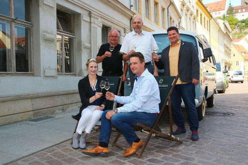 Stoßen vor der Weinbar Vinolovio am Theaterplatz schon mal aufs Weinfest an: Die frisch gekrönte Sächsische Weinprinzessin Ann-Kathrin Schatzl, Vinolovio-Mitbetreiber Reinhard Kremtz, Oberbürgermeister Olaf Raschke (m.), Winzer Ricco Hänsch (sitzend) und Uwe Reichel vom Gewerbeverein (r.). Foto: Farrar