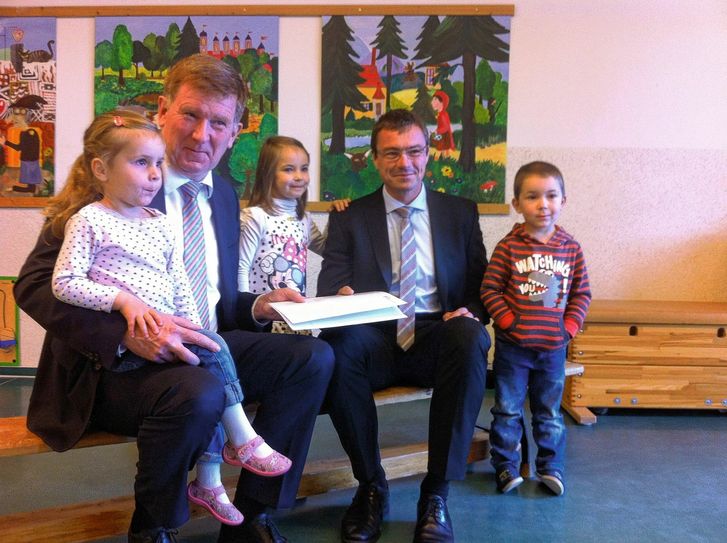 Kultus-Staatssekretär, Dr. Frank Pfeil (li.) übergab dern Förderbescheid an Ralf Rother (re.) mit Kindern der Kita. Foto: PR
