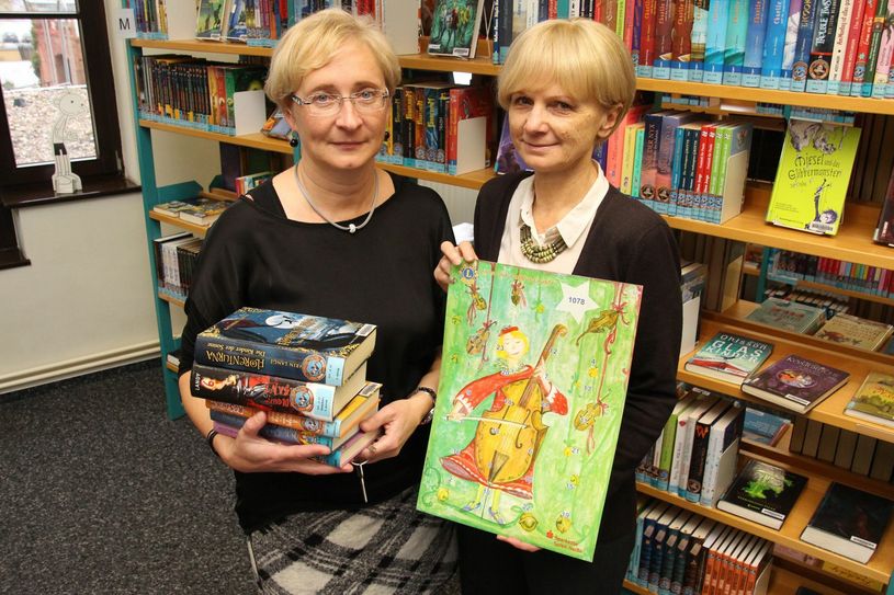 Heike Schumann (re.) von den Lions präsentiert den aktuellen Adventskalender. Annette Kornek von der Stadtbibliothek freut sich über die neuen Bücher, die angeschafft wurden. Foto: jho