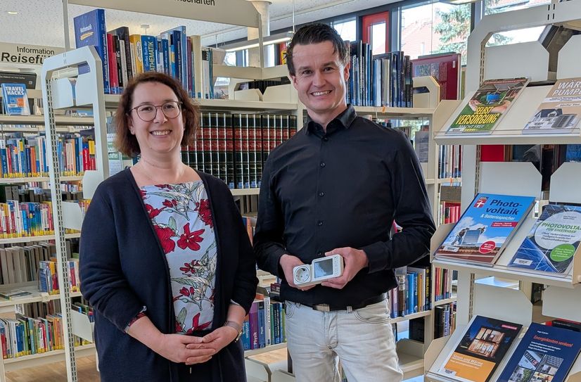 Energiemanager Matthias Herfter übergibt Stadtbibliotheksleiterin Manuela Mütze ein Strom-Messgerät.