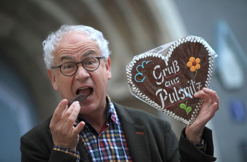 Schauspieler und Kabarettist Tom Pauls hält einen Pfefferkuchen in seiner linken Hand. In seiner rechten Hand hat er eine Gefüllte Spitze,  in die er sogleich reinbeißen mag. Damit macht er nicht nur Appetit, sondern Lust auf mehr. Der 65-Jährige Mime ist im Jahr 2024 Schirmherr bzw. Pate für den 20. Pfefferkuchenmarkt in Pulsnitz.