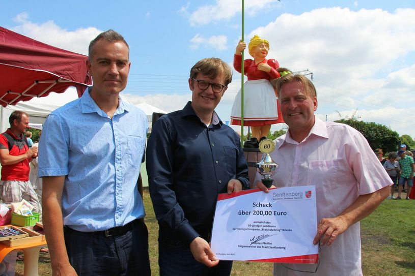 Veit Florczak (re.), Vereinsvorsitzende der Kleingartensparte »Franz Mehring« e.V. in Brieske, freut sich über die Glückwünsche zum 60-jährigen Jubiläum von Bürgermeister Andreas Pfeiffer (Mitte) und Ortsvorsteher Tino Balzer (li.). Im Hintergrund strahlt die ehemalige Marktfrau »Marga« jetzt als »Franzi« mit neuem Farbanstrich.