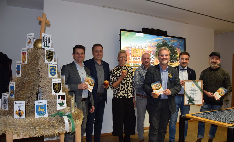 Neben der Erntekrone als Staffelstab stehen (v.l.) Marko Klimann und Bürgermeister Mirko Pink mit anderen Mitgliedern des Vorbereitungsteams.